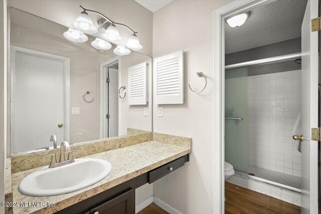 bathroom with hardwood / wood-style flooring, toilet, vanity, a textured ceiling, and walk in shower