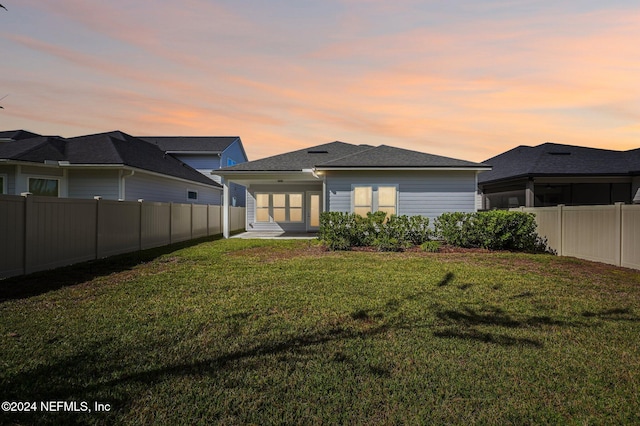 back house at dusk featuring a lawn