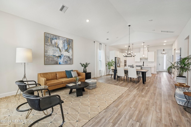 living room with lofted ceiling, a chandelier, and light hardwood / wood-style flooring