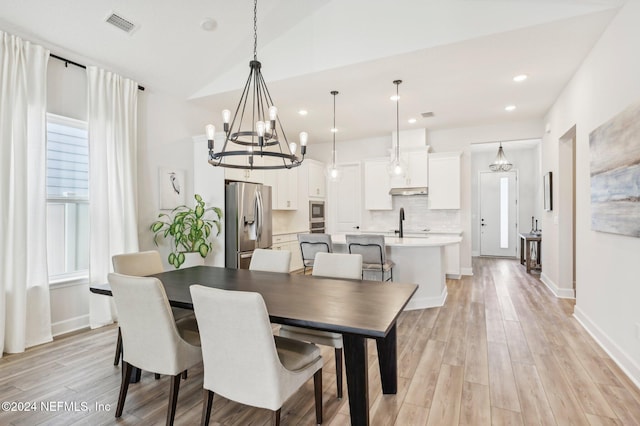 dining area with sink, light hardwood / wood-style floors, a notable chandelier, and lofted ceiling