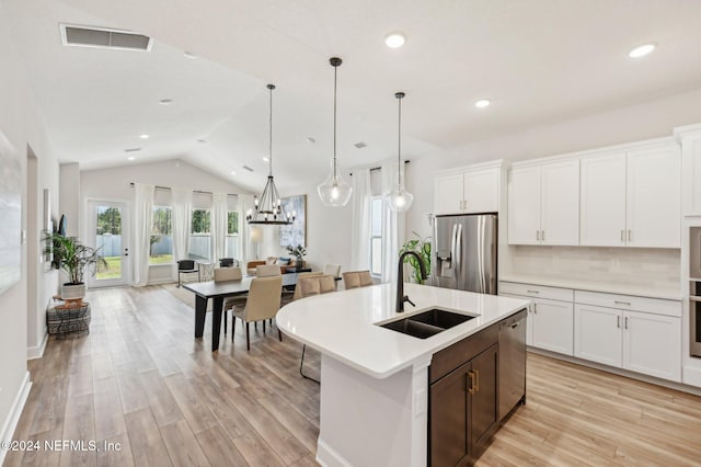 kitchen featuring lofted ceiling, appliances with stainless steel finishes, white cabinetry, decorative light fixtures, and sink