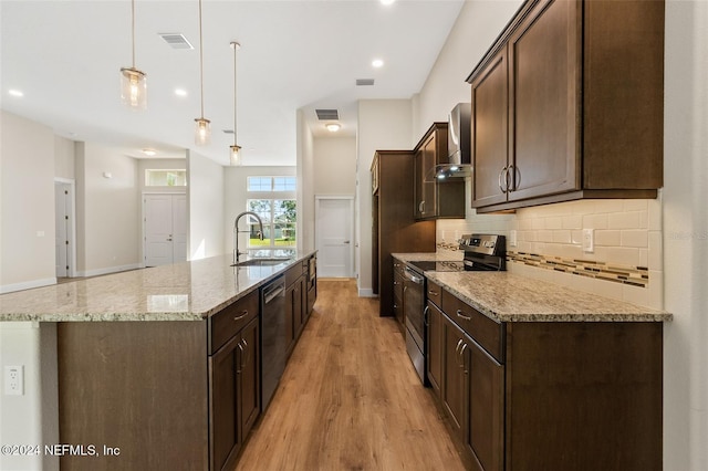 kitchen with light stone countertops, appliances with stainless steel finishes, light hardwood / wood-style floors, decorative light fixtures, and a kitchen island with sink