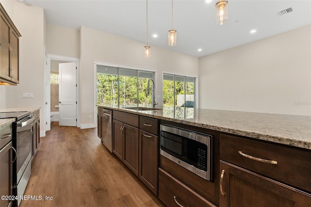 kitchen with hanging light fixtures, light stone countertops, light hardwood / wood-style flooring, sink, and stainless steel appliances