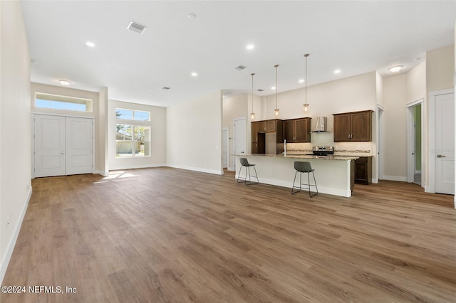 kitchen featuring wall chimney range hood, hanging light fixtures, a breakfast bar area, a kitchen island with sink, and wood-type flooring