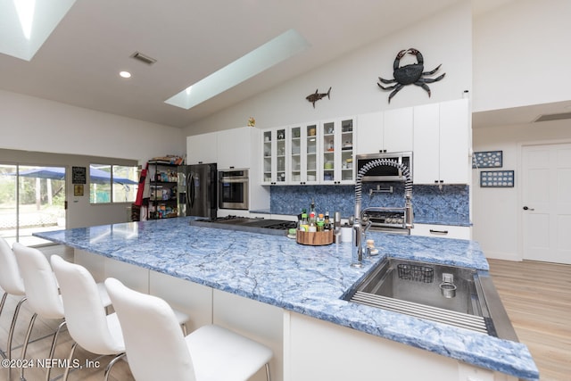 kitchen featuring white cabinets, stainless steel appliances, a skylight, and a kitchen breakfast bar