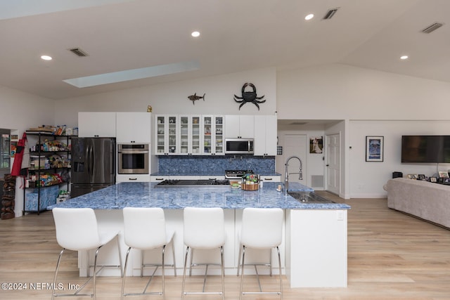 kitchen featuring appliances with stainless steel finishes, sink, white cabinetry, light hardwood / wood-style floors, and a breakfast bar area