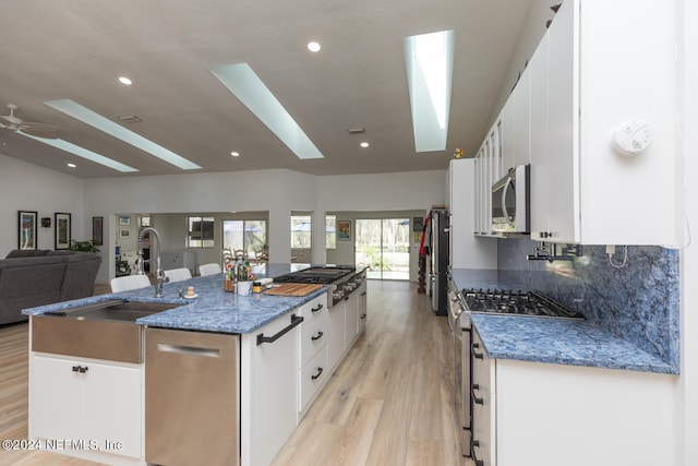 kitchen with appliances with stainless steel finishes, sink, a large island, light hardwood / wood-style floors, and white cabinets