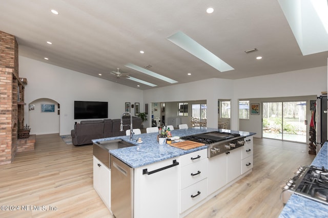 kitchen featuring sink, white cabinetry, stainless steel appliances, vaulted ceiling with skylight, and a kitchen island with sink