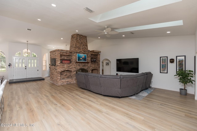 living room featuring light hardwood / wood-style floors, vaulted ceiling with skylight, a brick fireplace, and ceiling fan