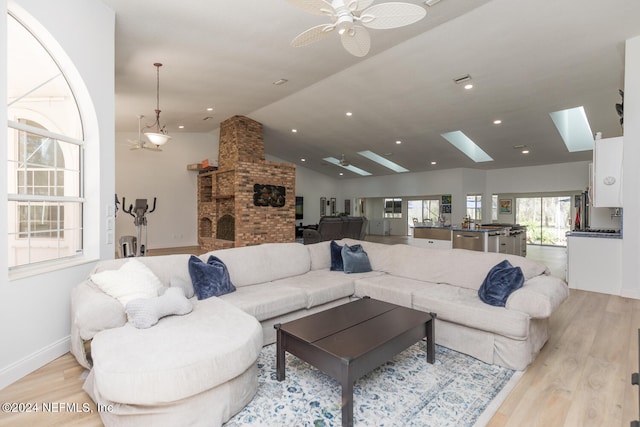 living room with vaulted ceiling with skylight, light hardwood / wood-style flooring, a fireplace, and ceiling fan