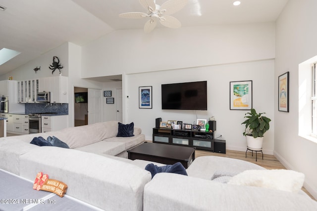 living room featuring a skylight, light hardwood / wood-style flooring, high vaulted ceiling, and ceiling fan