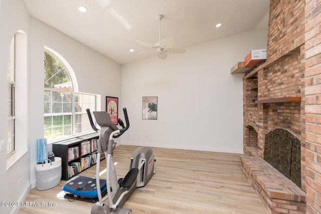 workout area with vaulted ceiling, light hardwood / wood-style flooring, a brick fireplace, and a healthy amount of sunlight