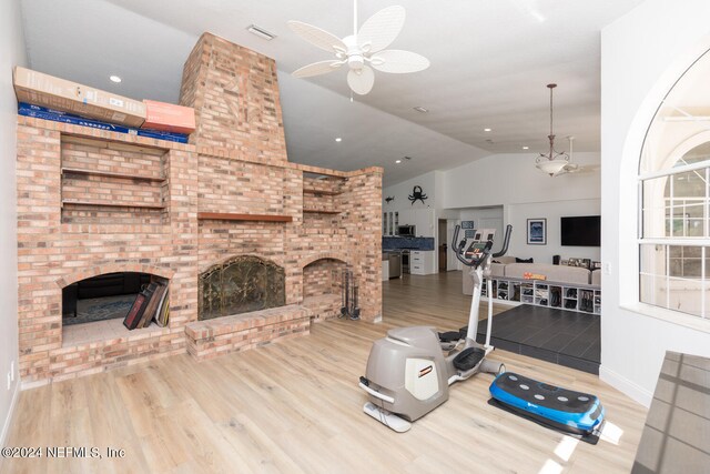 exercise area with light hardwood / wood-style floors, ceiling fan, vaulted ceiling, and a brick fireplace