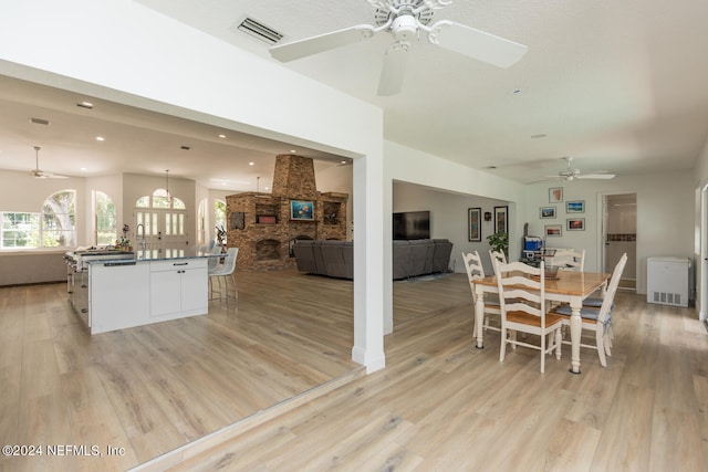 dining space featuring light hardwood / wood-style floors, a brick fireplace, and ceiling fan