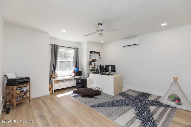 office space with ceiling fan, an AC wall unit, and light wood-type flooring