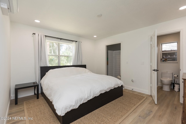 bedroom featuring connected bathroom, hardwood / wood-style flooring, and multiple windows