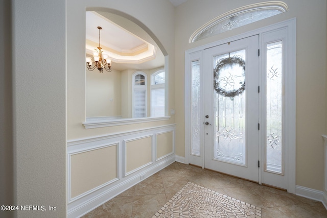 foyer featuring crown molding, an inviting chandelier, and a raised ceiling