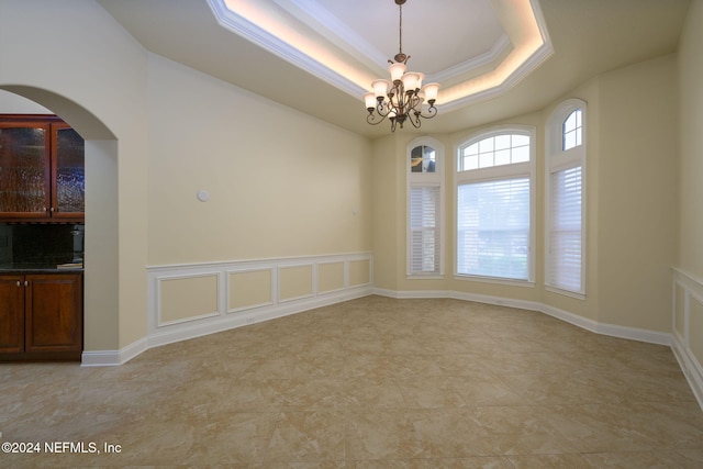 unfurnished room with an inviting chandelier, ornamental molding, and a tray ceiling