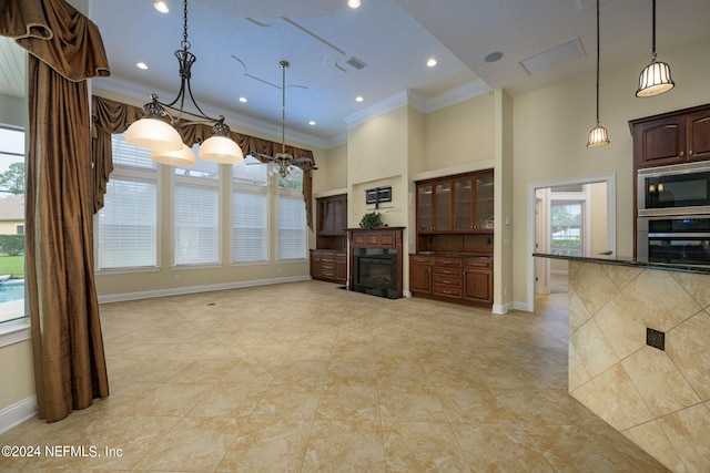 kitchen featuring a towering ceiling, stainless steel appliances, decorative light fixtures, crown molding, and a notable chandelier