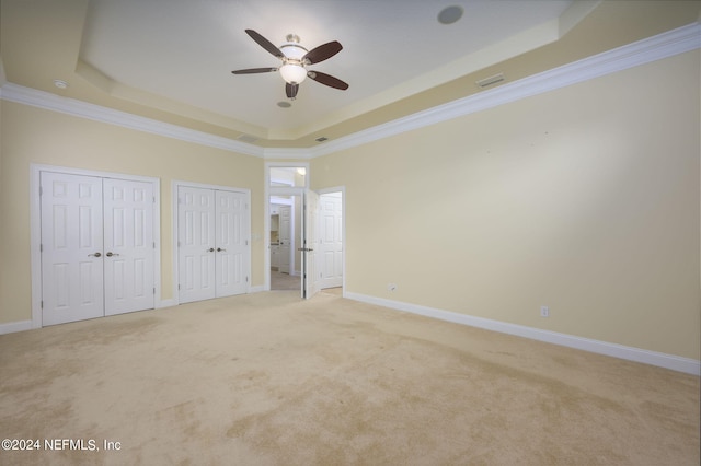 unfurnished bedroom featuring ornamental molding, light carpet, ceiling fan, and a raised ceiling