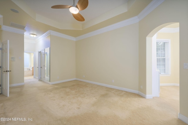 empty room featuring light carpet, ornamental molding, a tray ceiling, and ceiling fan