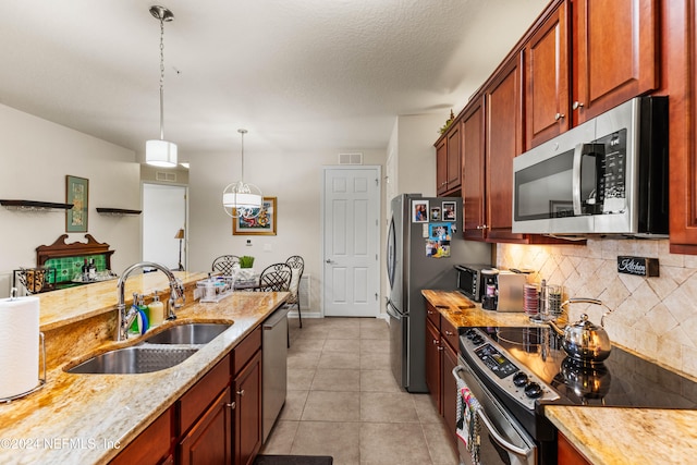 kitchen featuring appliances with stainless steel finishes, light tile patterned floors, pendant lighting, light stone countertops, and sink