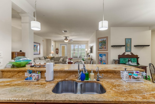 kitchen featuring ceiling fan, sink, decorative light fixtures, and light stone counters