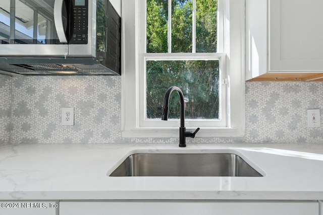 details with light stone countertops, sink, backsplash, and white cabinets