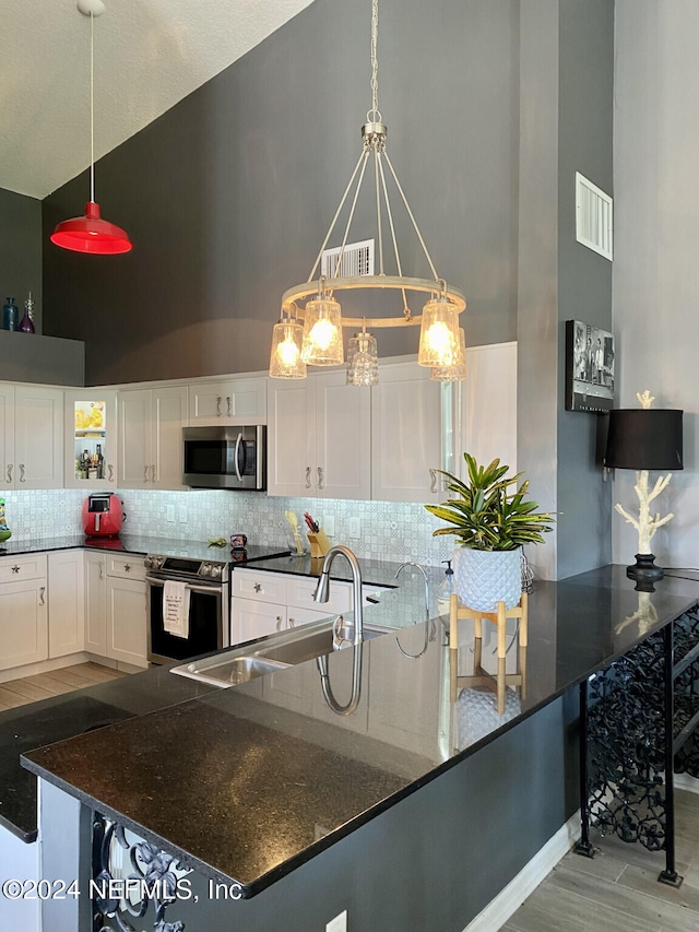 kitchen featuring appliances with stainless steel finishes, light wood-type flooring, white cabinetry, decorative light fixtures, and high vaulted ceiling