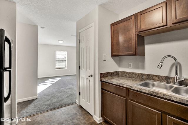 kitchen featuring stainless steel fridge, sink, dark colored carpet, and a textured ceiling