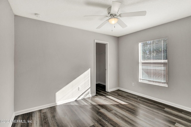 unfurnished bedroom featuring dark wood-type flooring, ceiling fan, a closet, and a walk in closet