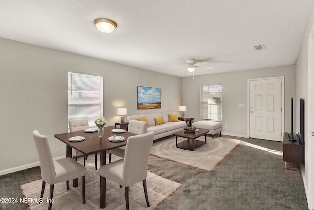 dining room with a wealth of natural light, dark colored carpet, and ceiling fan