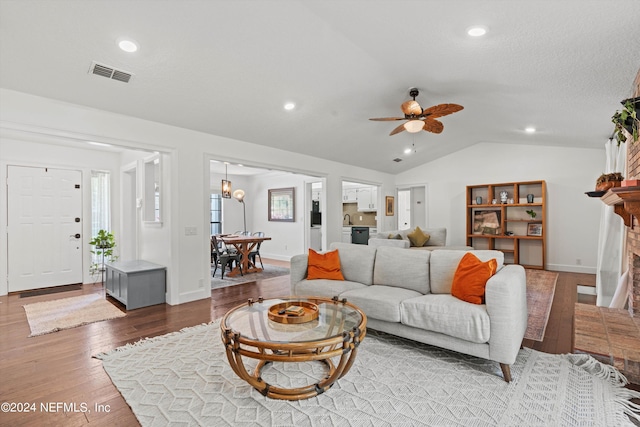 living room featuring sink, hardwood / wood-style floors, vaulted ceiling, a fireplace, and ceiling fan with notable chandelier