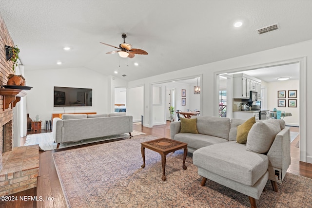 living room featuring ceiling fan, wood-type flooring, a fireplace, and vaulted ceiling