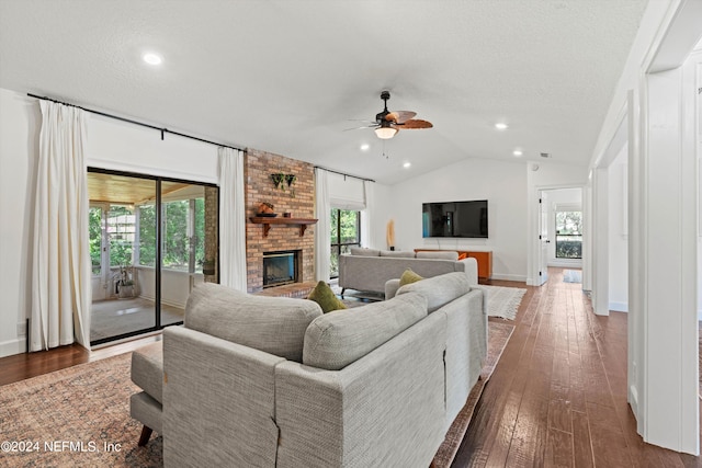 living room with ceiling fan, a textured ceiling, vaulted ceiling, dark hardwood / wood-style floors, and a fireplace