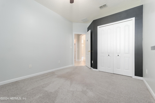 unfurnished bedroom with a closet, a textured ceiling, light colored carpet, and ceiling fan