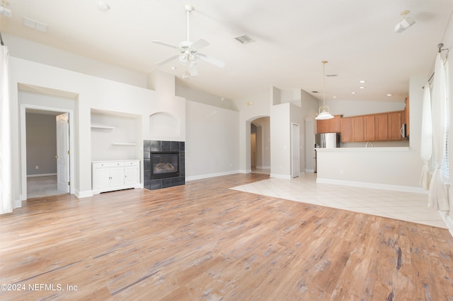 unfurnished living room with high vaulted ceiling, a tile fireplace, light wood-type flooring, and ceiling fan