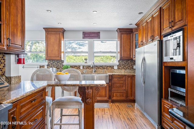 kitchen featuring light wood-type flooring, light stone countertops, stainless steel appliances, and a healthy amount of sunlight