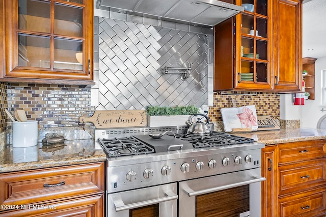 kitchen featuring exhaust hood, decorative backsplash, light stone counters, and high end stove