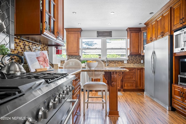 kitchen featuring light stone countertops, a kitchen bar, light wood-type flooring, backsplash, and stainless steel appliances