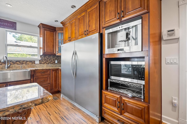 kitchen featuring light stone counters, backsplash, sink, light hardwood / wood-style floors, and stainless steel appliances