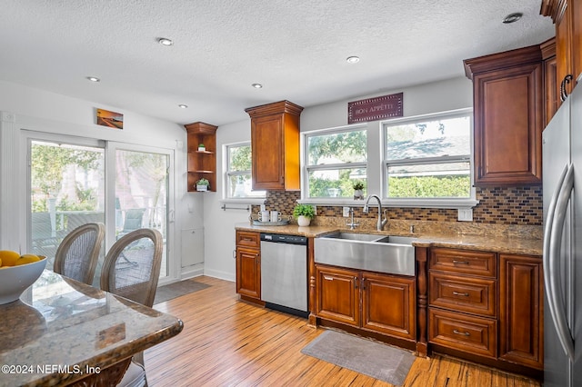 kitchen with tasteful backsplash, light stone counters, appliances with stainless steel finishes, light wood-type flooring, and sink