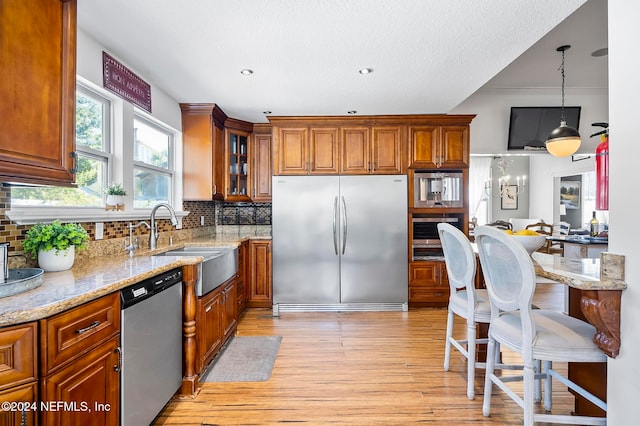 kitchen featuring decorative backsplash, light hardwood / wood-style flooring, stainless steel appliances, sink, and decorative light fixtures