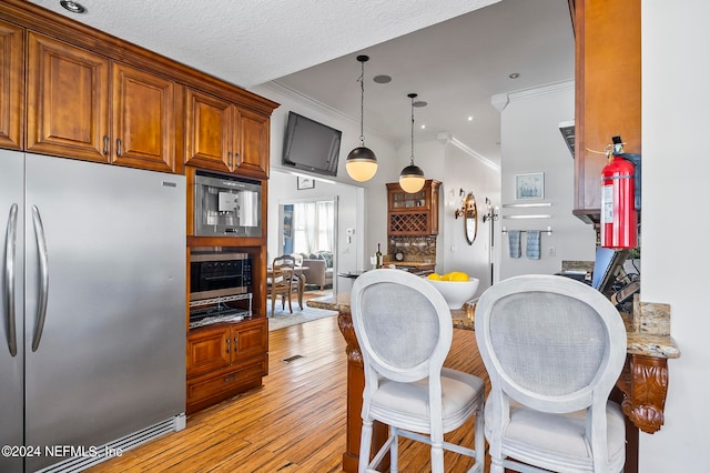 kitchen with appliances with stainless steel finishes, a textured ceiling, hanging light fixtures, light hardwood / wood-style floors, and crown molding