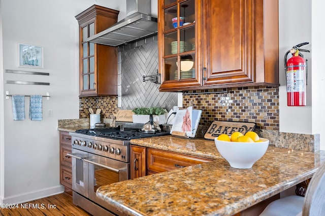 kitchen with dark hardwood / wood-style flooring, backsplash, light stone countertops, stainless steel stove, and wall chimney exhaust hood