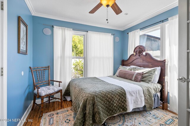 bedroom featuring ceiling fan, wood-type flooring, multiple windows, and ornamental molding