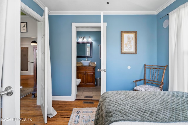 bedroom featuring ensuite bath, wood-type flooring, and ornamental molding