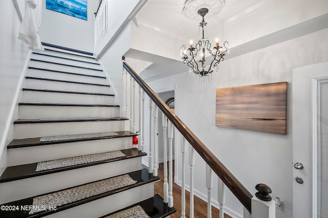 stairway featuring crown molding, hardwood / wood-style flooring, and an inviting chandelier