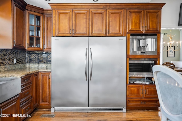 kitchen with tasteful backsplash, light stone counters, a chandelier, light hardwood / wood-style floors, and stainless steel appliances