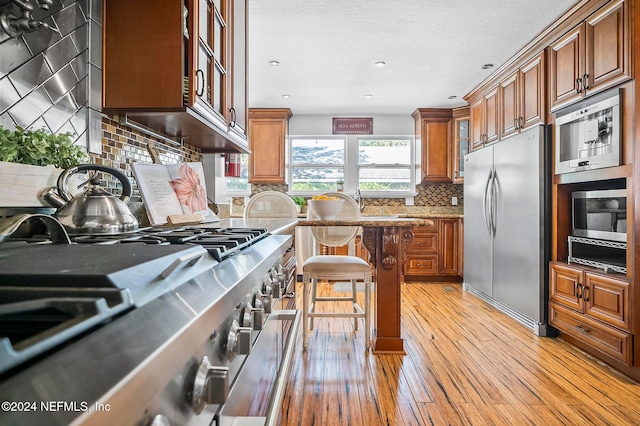 kitchen featuring decorative backsplash, a kitchen bar, light wood-type flooring, appliances with stainless steel finishes, and a textured ceiling